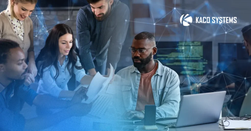 An image that represents the title and theme of this blog: In-House IT vs. Outsourced IT vs. Co-Managed: A Practical Guide. A group of people sit at a large conference table in an office, surrounded by laptops and other technology.
